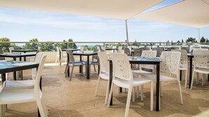 Eine Terrasse im Freien mit Tischen und Stühlen, strahlend blauer Himmel und Blick auf das Meer.