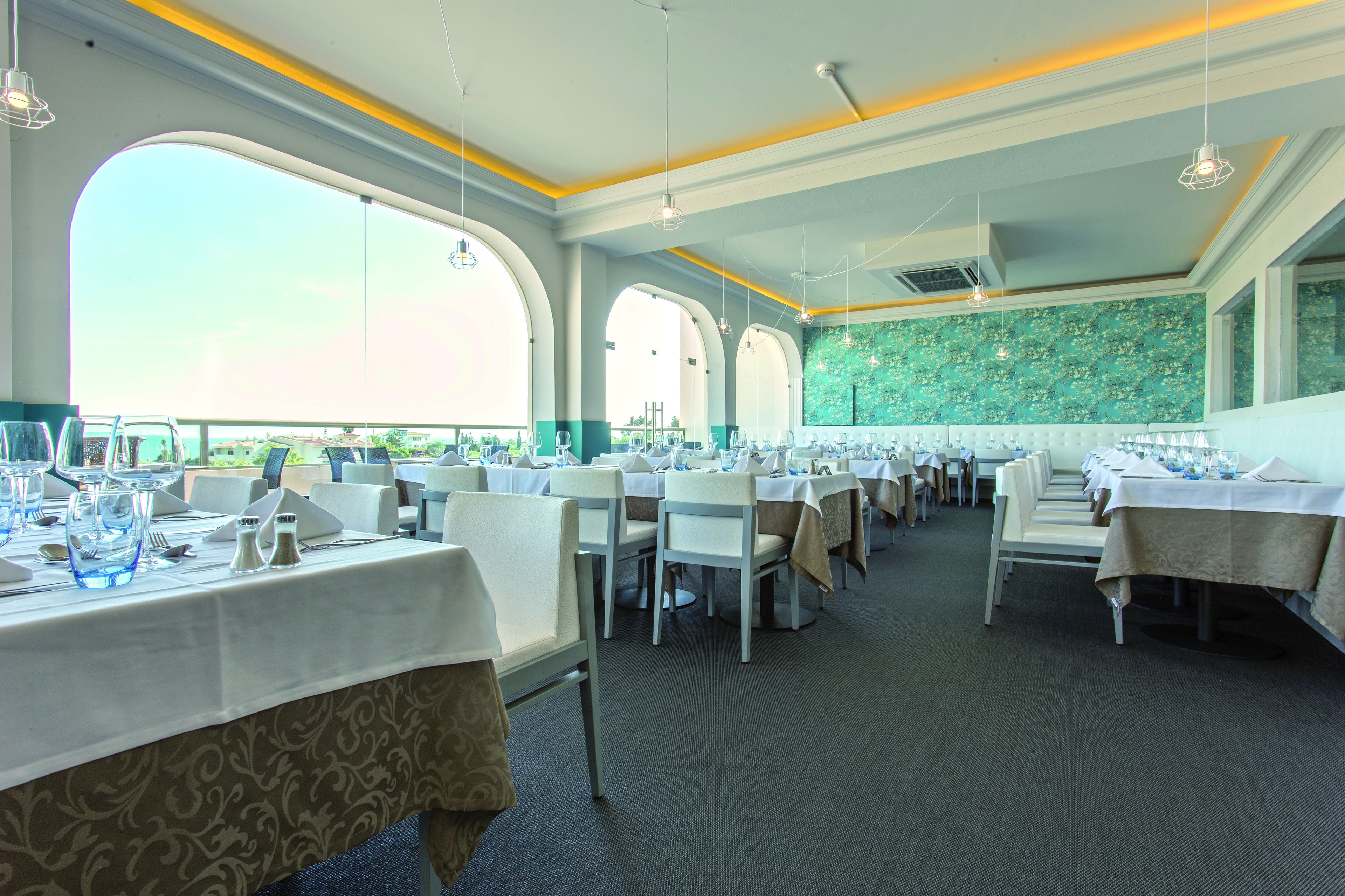 Un restaurante con varias mesas dispuestas para comer, ventanas amplias y una pared con azulejos verdes.