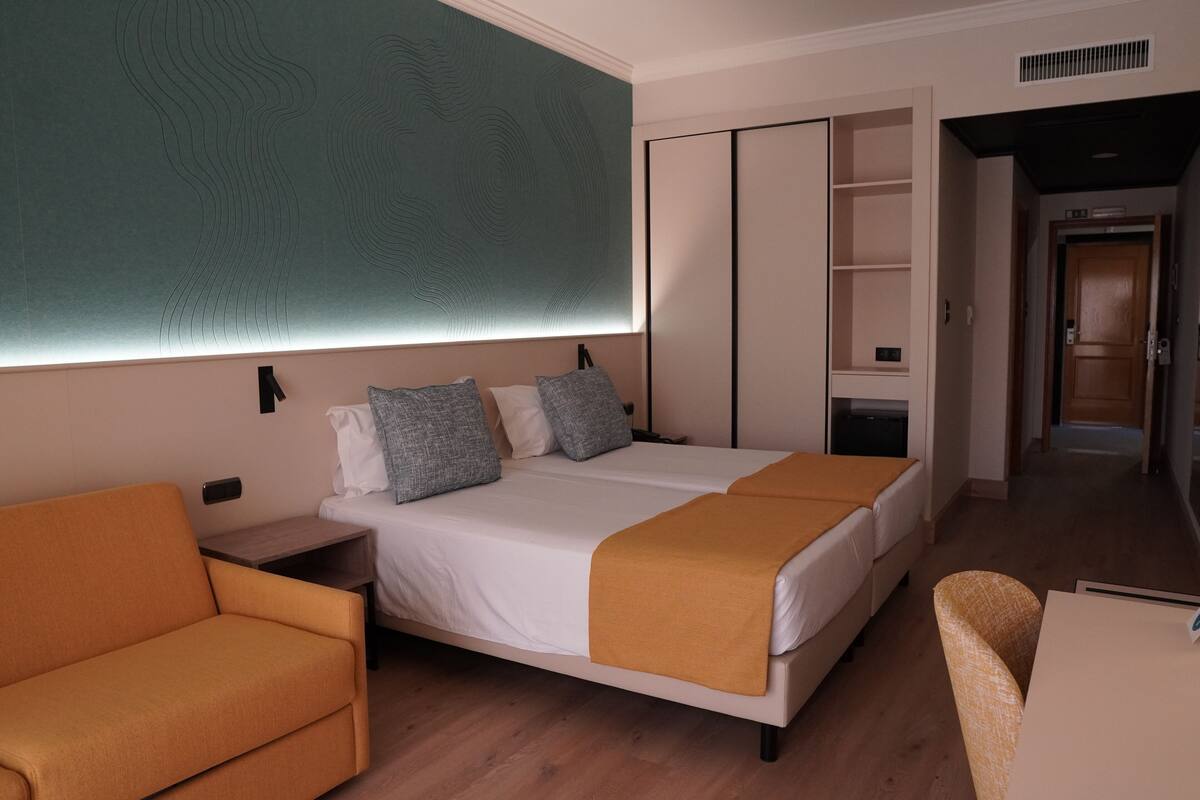 A modern hotel room with a large bed, a sofa, a desk, and a wardrobe.