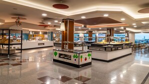 Eine moderne Cafeteria mit mehreren Speiseausgaben, einem zentralen Servicetheke und einer Sitzgelegenheit mit Tischen und Stühlen.