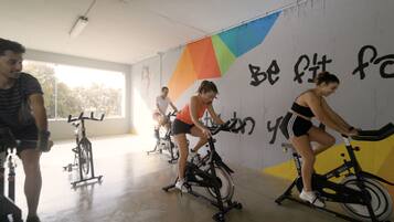 Un grupo de personas ejercitándose en bicicletas estáticas en un gimnasio con decoración motivacional en las paredes y amplias ventanas.