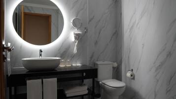 Un baño moderno con un espejo redondo, lavamanos blanco y un inodoro.