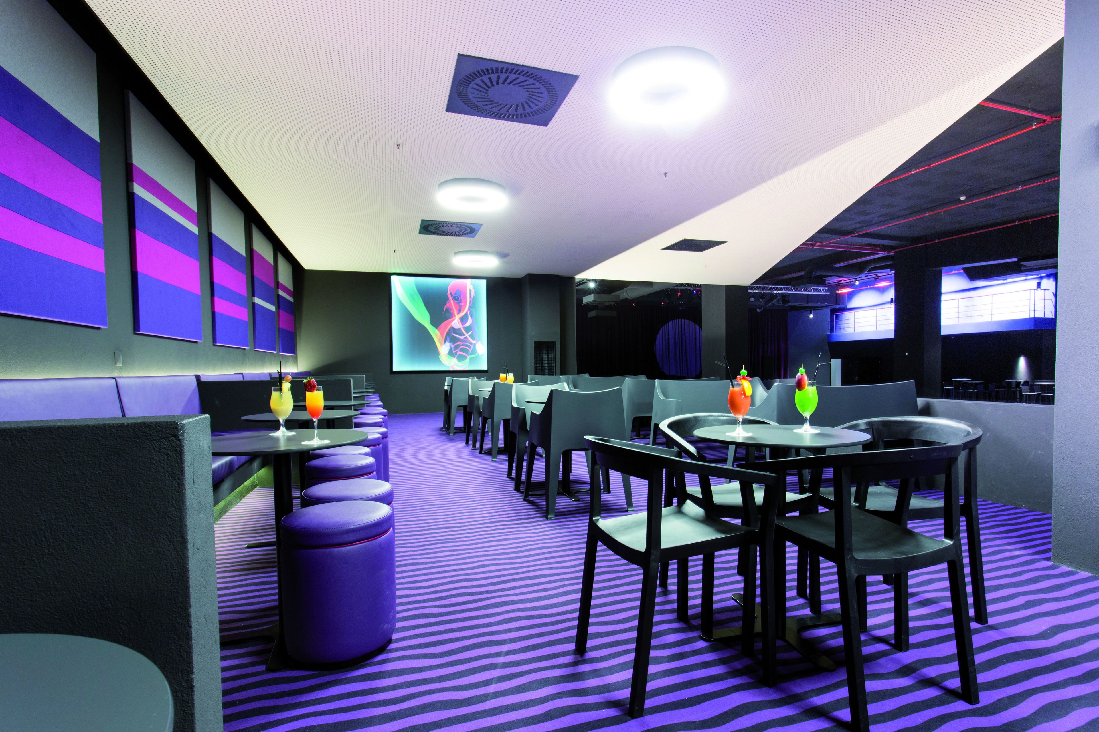 Un restaurant modern amb una catifa de ratlles morades, cadires negres i grises i taules.