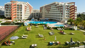 Ein Hotel mit mehreren Etagen, einem zentral gelegenen Schwimmbad und Außenbereichen zum Entspannen mit Liegestühlen und Sonnenschirmen.