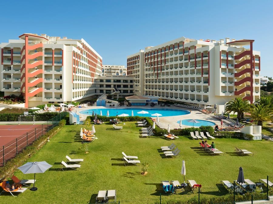 A hotel with multiple floors, a central swimming pool, and outdoor lounge areas with sun loungers and umbrellas.