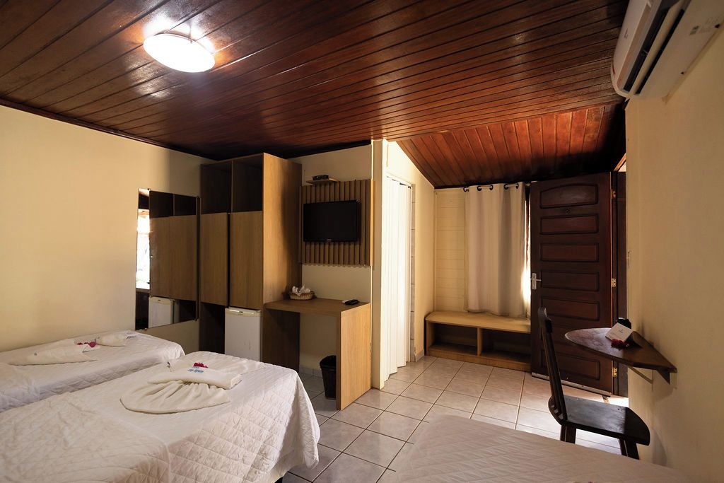 A hotel room with two beds, a desk, a television, and a shower area.