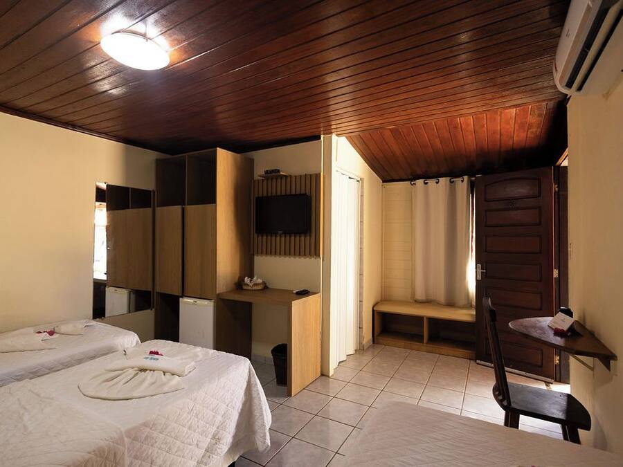 Quarto de hotel com duas camas, uma mesa, televisão e chuveiro.