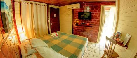 A room with a checkered bedspread, a television mounted on a brick wall, and a small table with items on it.