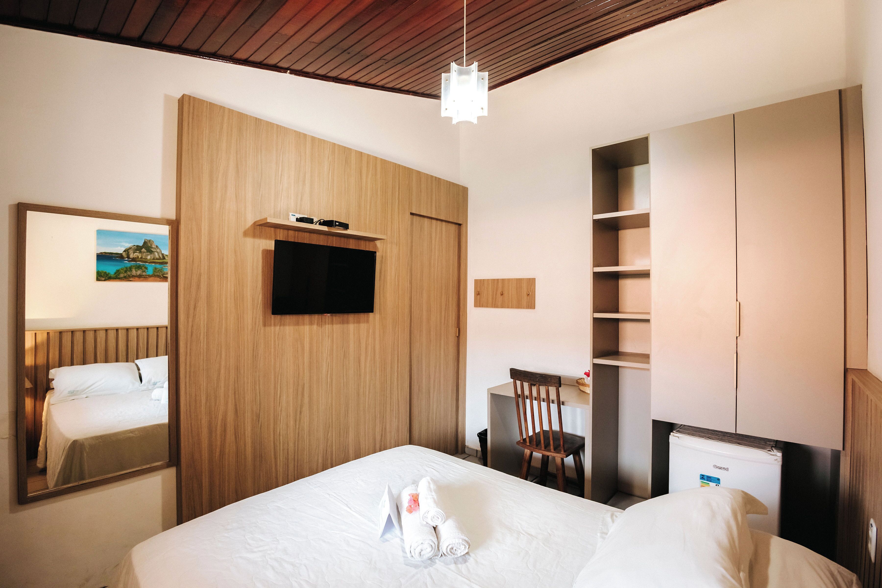 A hotel room with a bed, a desk, a chair, a TV, and a wardrobe.
