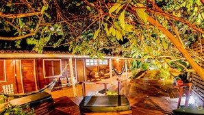 A wooden deck with a hammock, a covered seating area, and a boat. - Pousada Lenda das Águas (Fernando de Noronha)