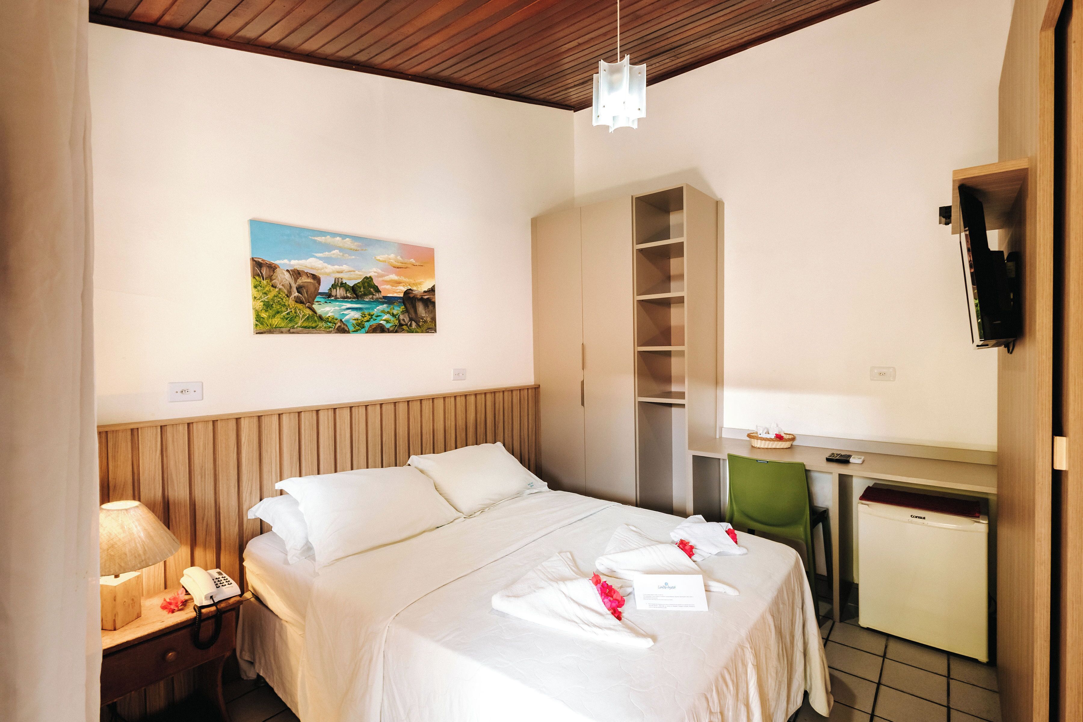 Une chambre d’hôtel avec un lit, un bureau, une chaise, un petit réfrigérateur, un tableau au mur et une lampe.