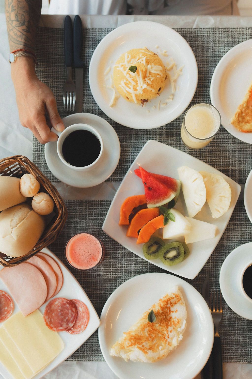 Una mesa de desayuno con platos de comida, una cesta de panes y una taza de café.