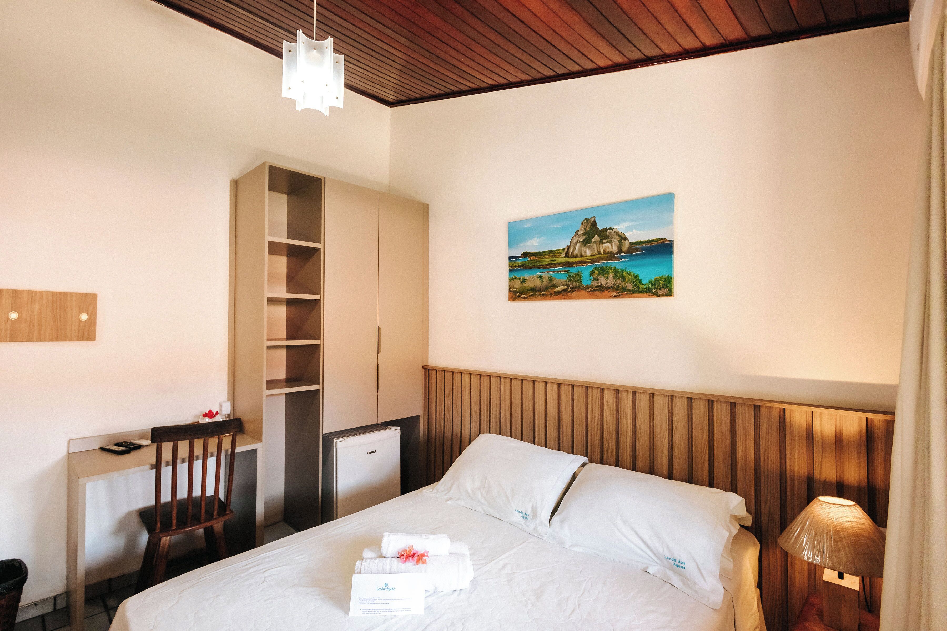 Habitación de hotel con cama, escritorio, silla, mesita, lámpara y un cuadro en la pared.
