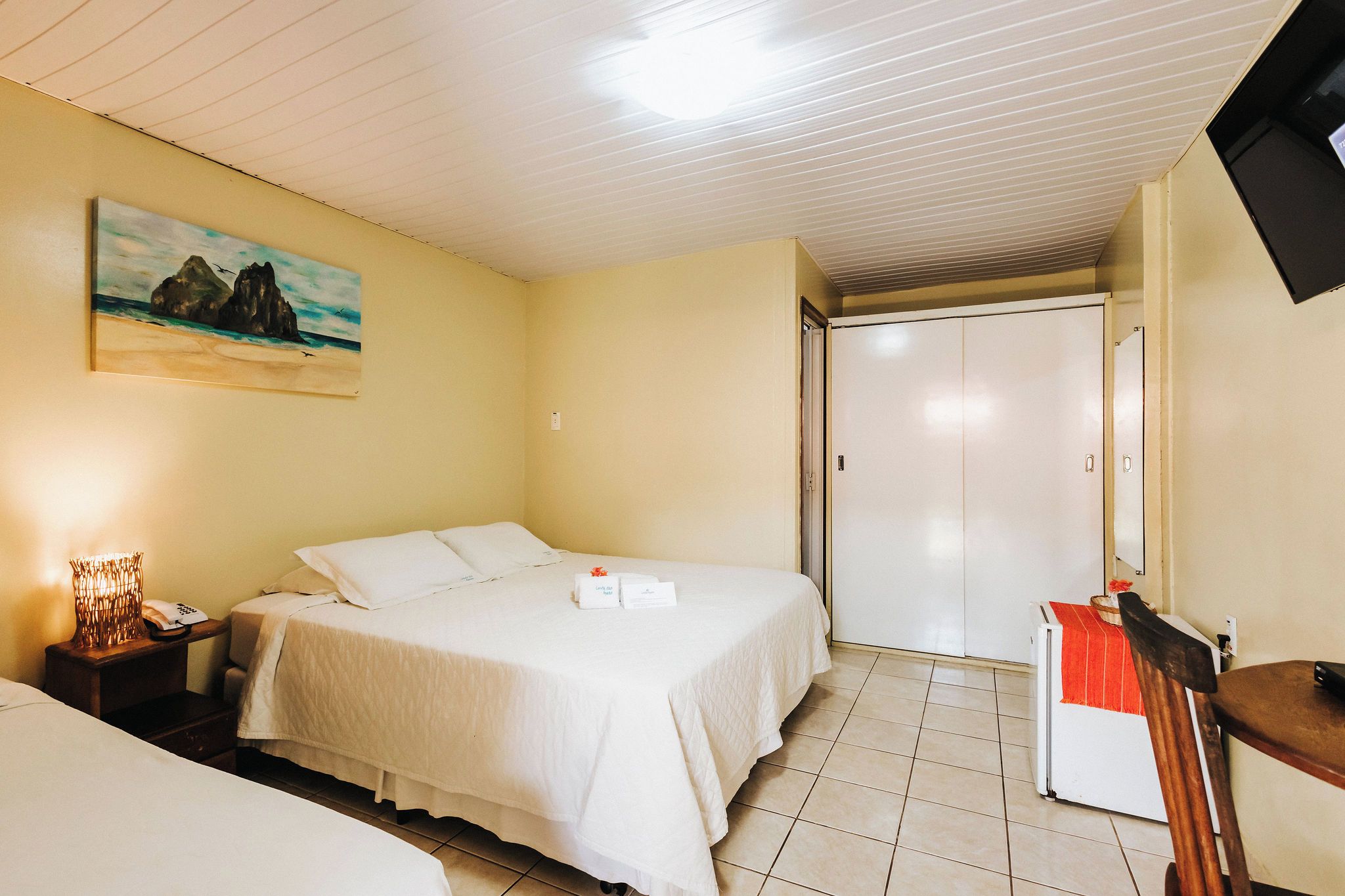 Una camera d'albergo con un letto, una scrivania, una sedia, una televisione e un quadro appeso al muro.