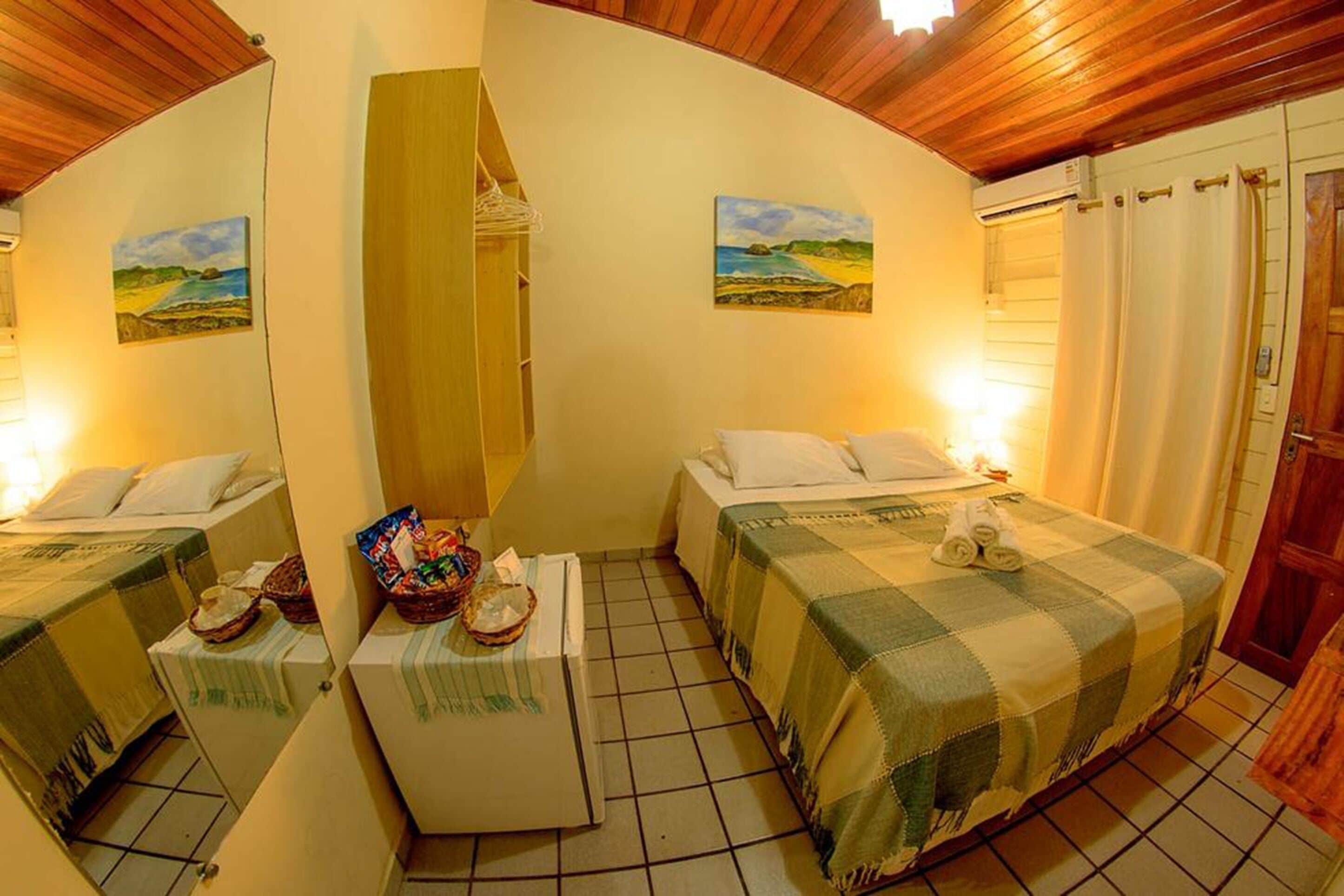 A room with two beds, a small table with a basket, and a painting on the wall.