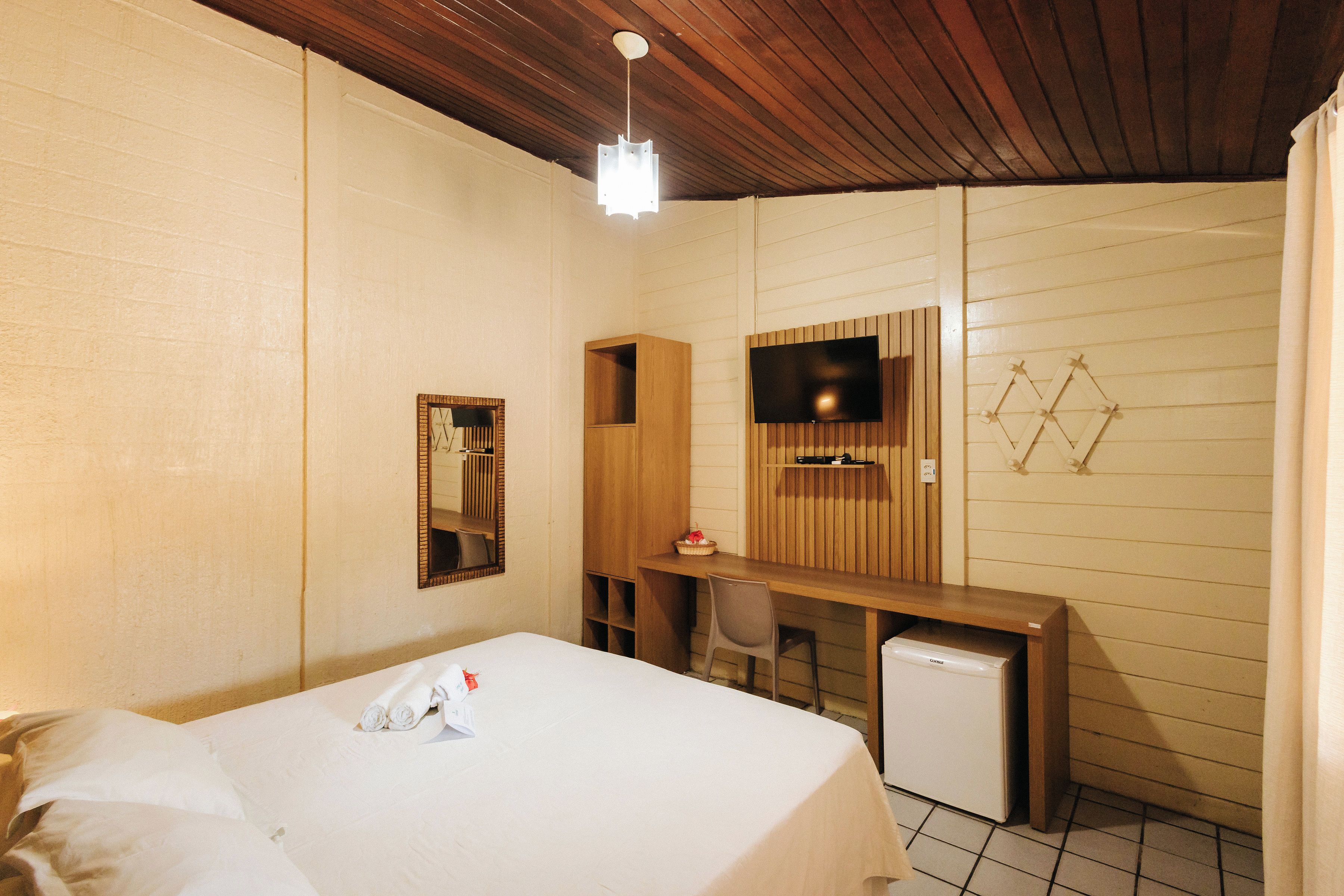 A hotel room with a bed, a desk, a chair, a television, and a small refrigerator.