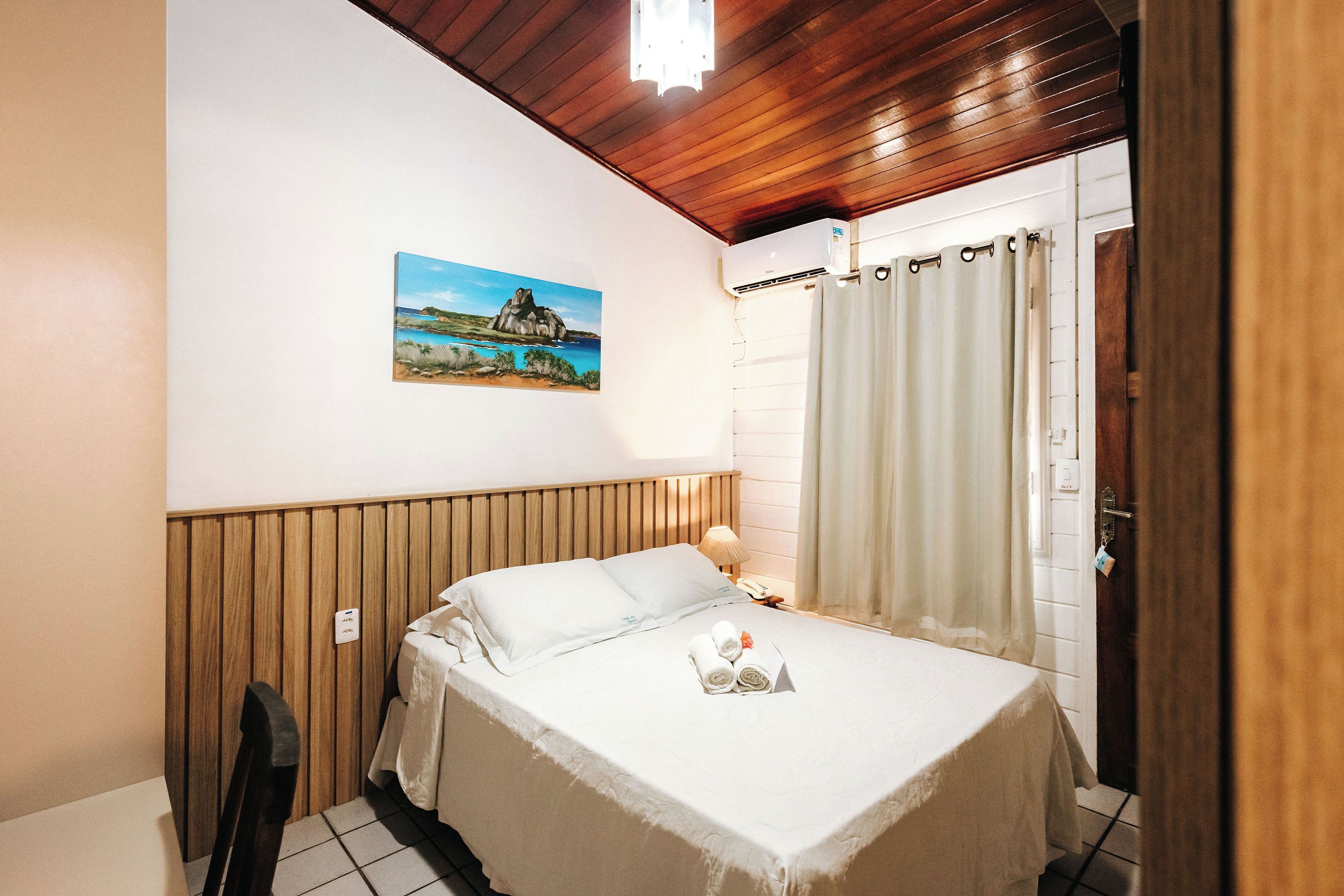 Habitación de hotel con cama, un cuadro en la pared, techo de madera y una ventana con cortinas.