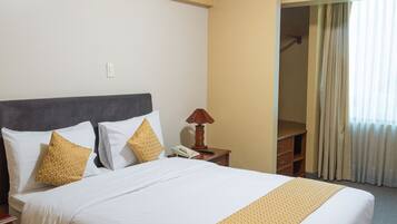 Una habitación de hotel con cama, mesita de noche, lámpara y armario.
