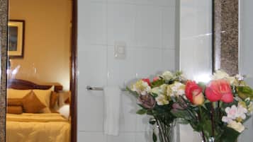 A bathroom with a granite countertop, a white sink, and a mirror reflecting a bed and a door.