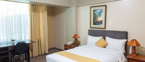 Una habitación de hotel con cama, escritorio, silla y dos lámparas de noche.