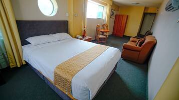 A hotel room with a large bed, a chair, a wardrobe, and a small table.