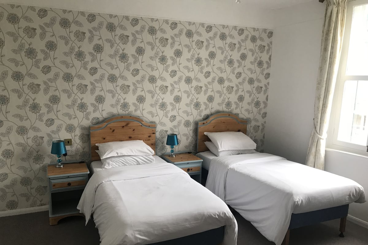 A twin room with two single beds, wooden headboards, bedside tables with lamps, and floral wallpaper.