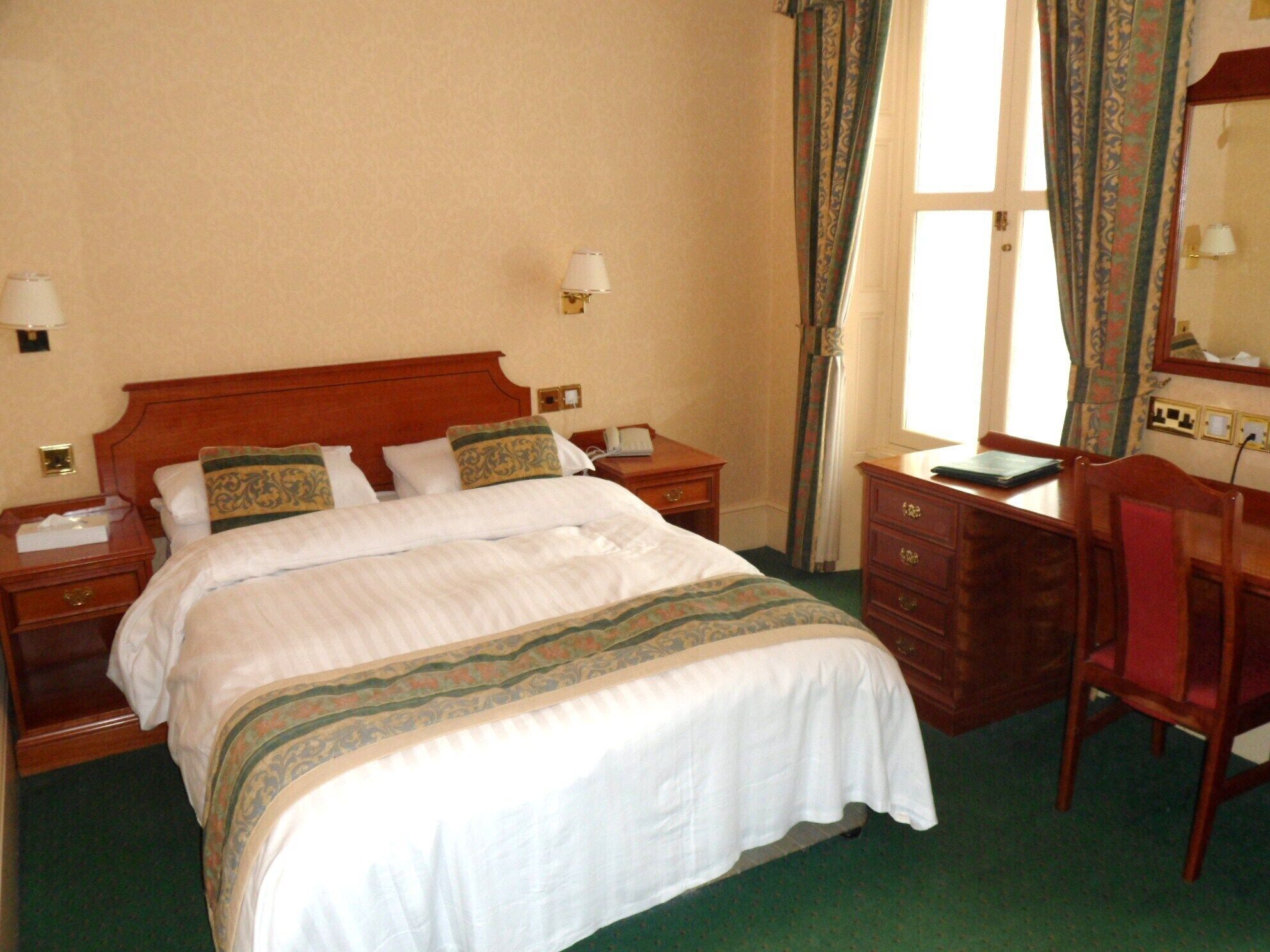 Een hotelkamer met een groot bed, twee nachtkastjes, een bureau en een stoel.