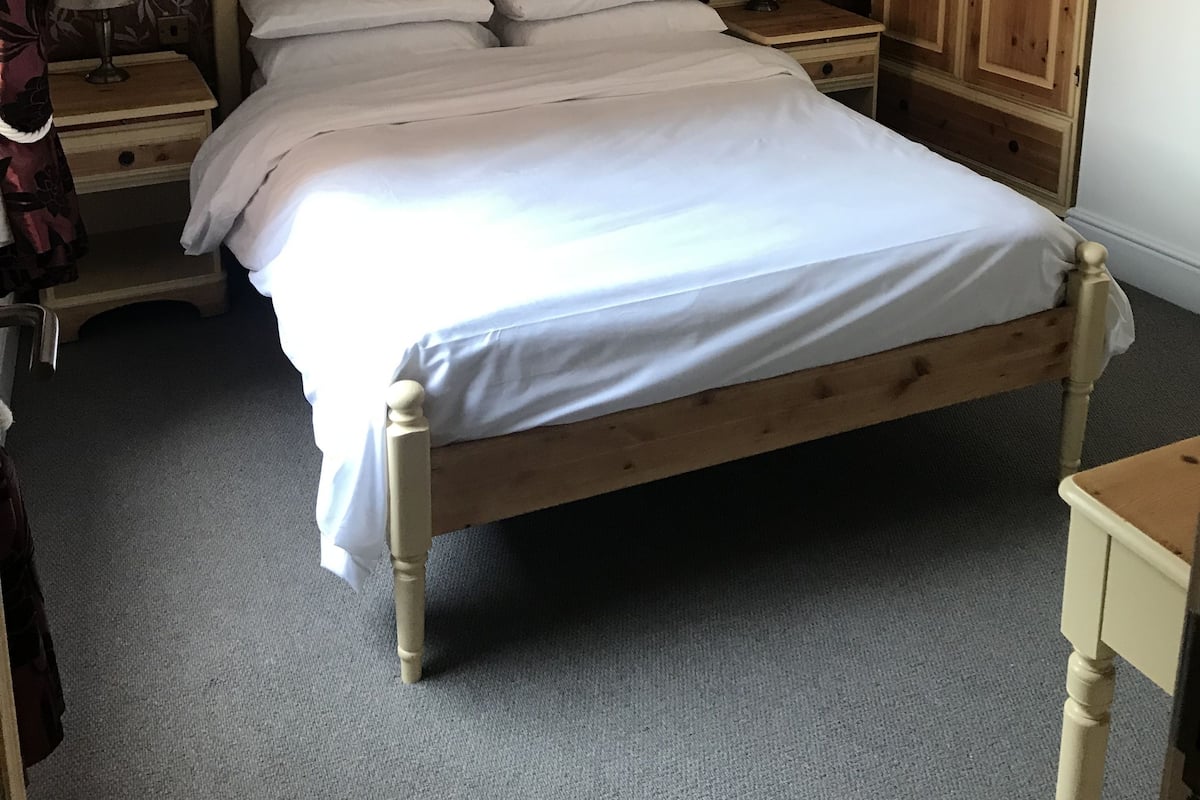 A bedroom with a wooden bed, a nightstand with a lamp, a wardrobe, and a patterned wallpaper.