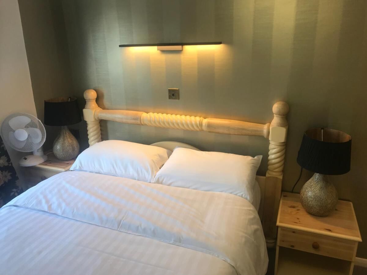 A neatly made bed with white linens, a wooden headboard, and two bedside tables with lamps and a fan.