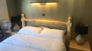 A neatly made bed with white linens, a wooden headboard, and two bedside tables with lamps and a fan.