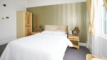 A hotel room with a large bed, a wooden wardrobe, a bedside table with a lamp, and a window with curtains.