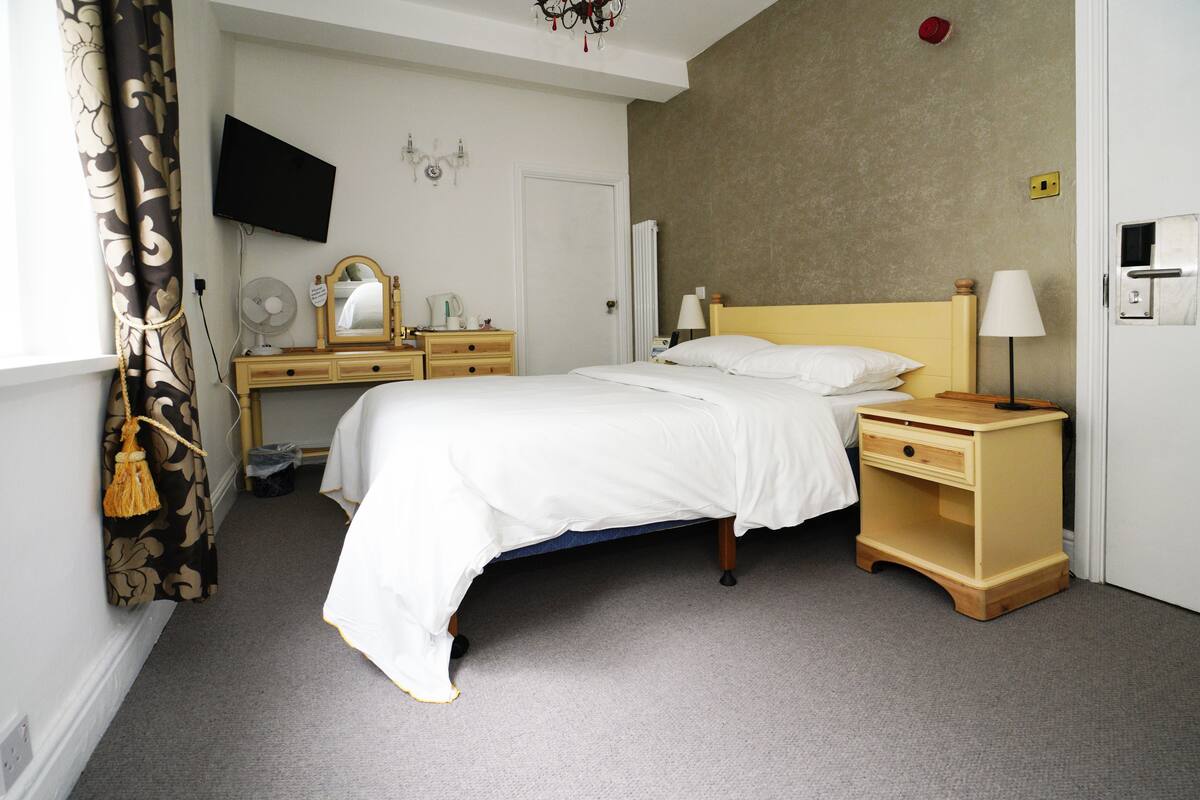 A hotel room with a bed, bedside tables, a TV mounted on the wall, and a window with curtains.