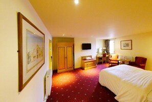 A hotel room with a bed, a desk with a chair, a television, and a wardrobe. - Three Queens Hotel (Burton on Trent)