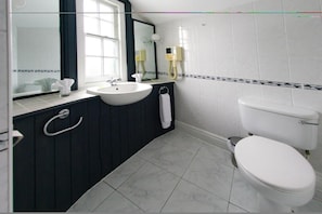 A bathroom with a white sink, dark wooden vanity, a white toilet, and a mirror with a black frame. - Three Queens Hotel (Burton on Trent)