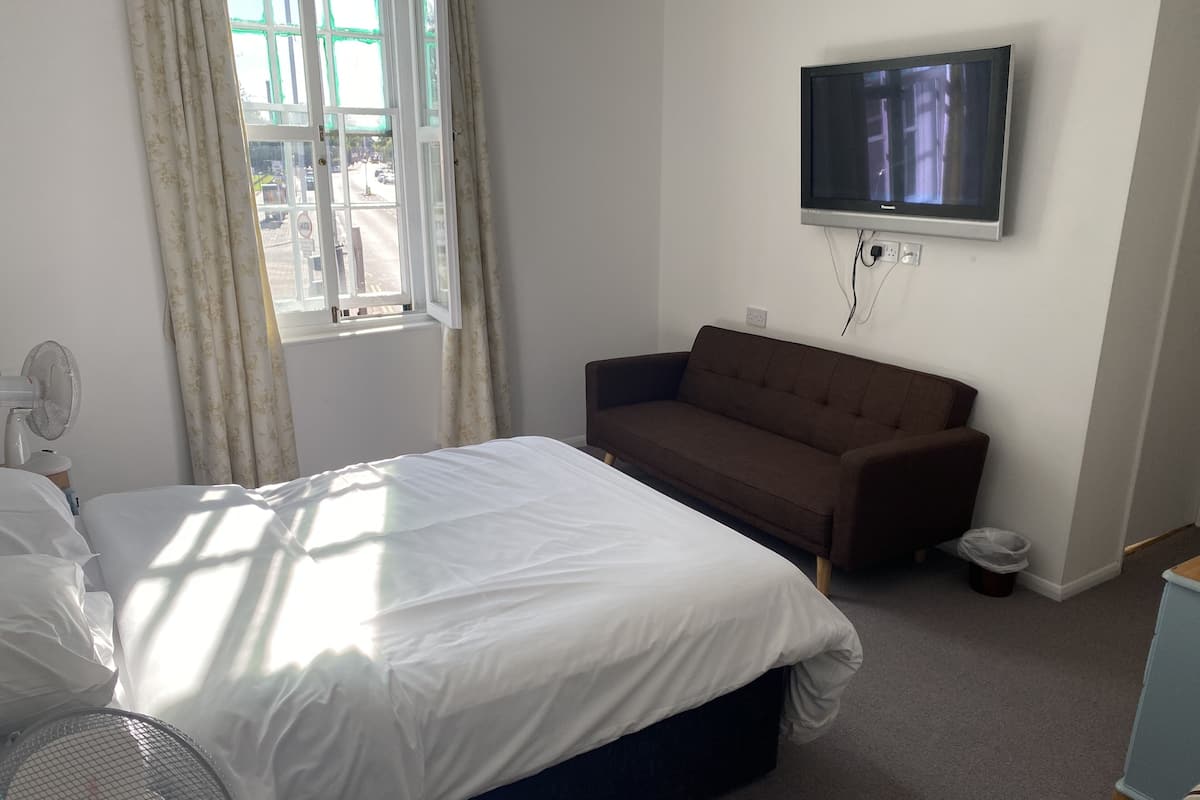 A hotel room with a bed, a sofa, a TV mounted on the wall, and a window with curtains.