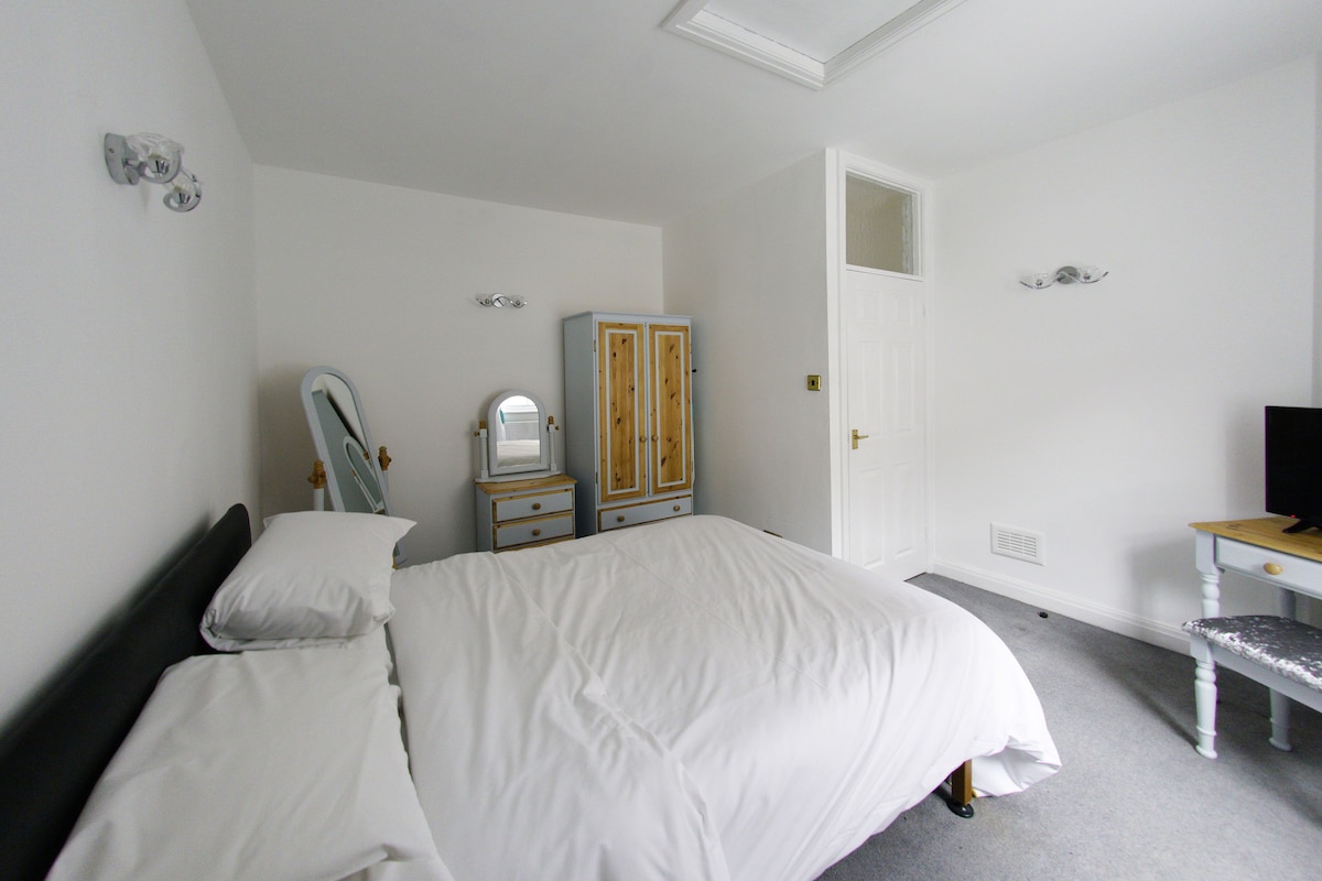 A bedroom with a bed, a dresser, a mirror, and a desk.