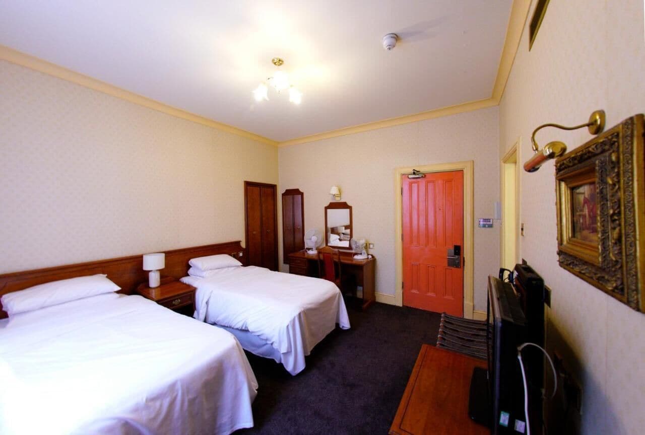 A hotel room with two single beds, a desk with a chair, a television, and a door leading to another room.