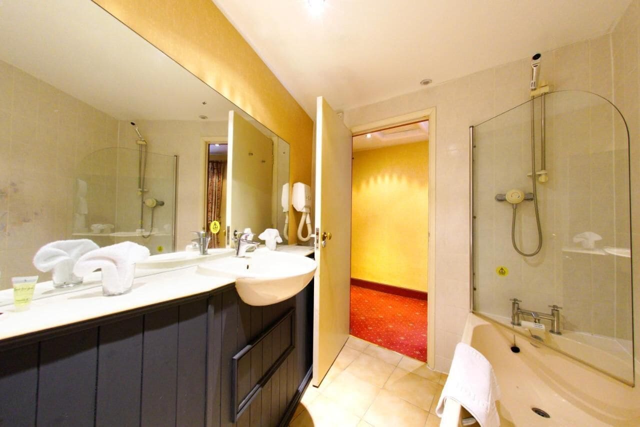 Een hotelbadkamer met twee wastafels, een grote spiegel, een douche en een rode gang met tapijt.