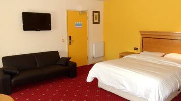 A hotel room with a bed, a sofa, a television mounted on the wall, and a door with a sign.