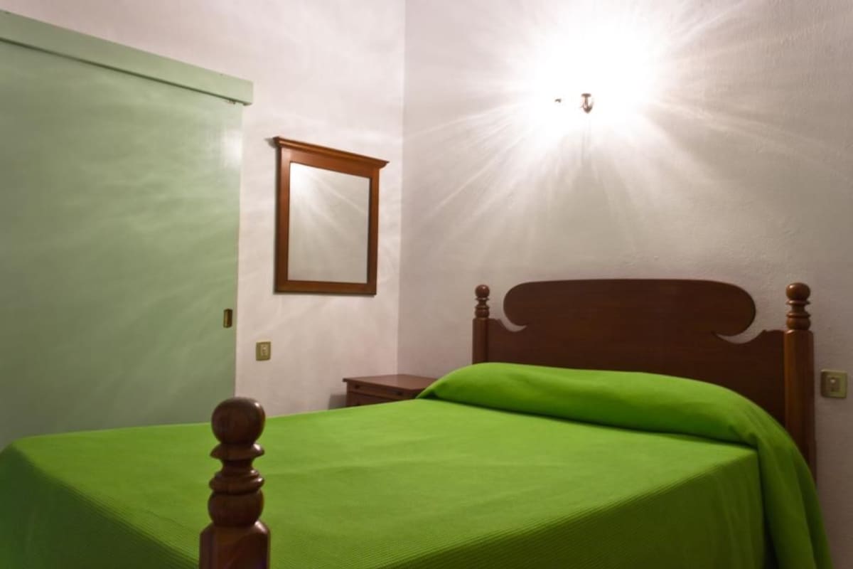 A single bed with a wooden headboard and a green bedspread in a room with white walls and a wooden door.