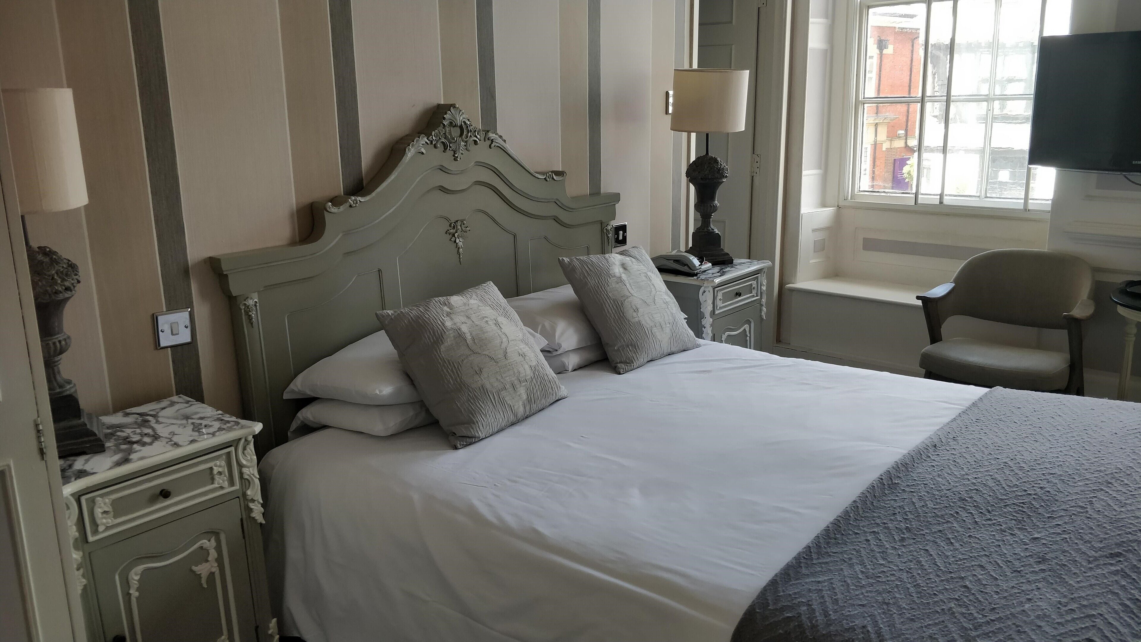 A neatly made bed with a headboard, two bedside tables with lamps, a chair, and a television.