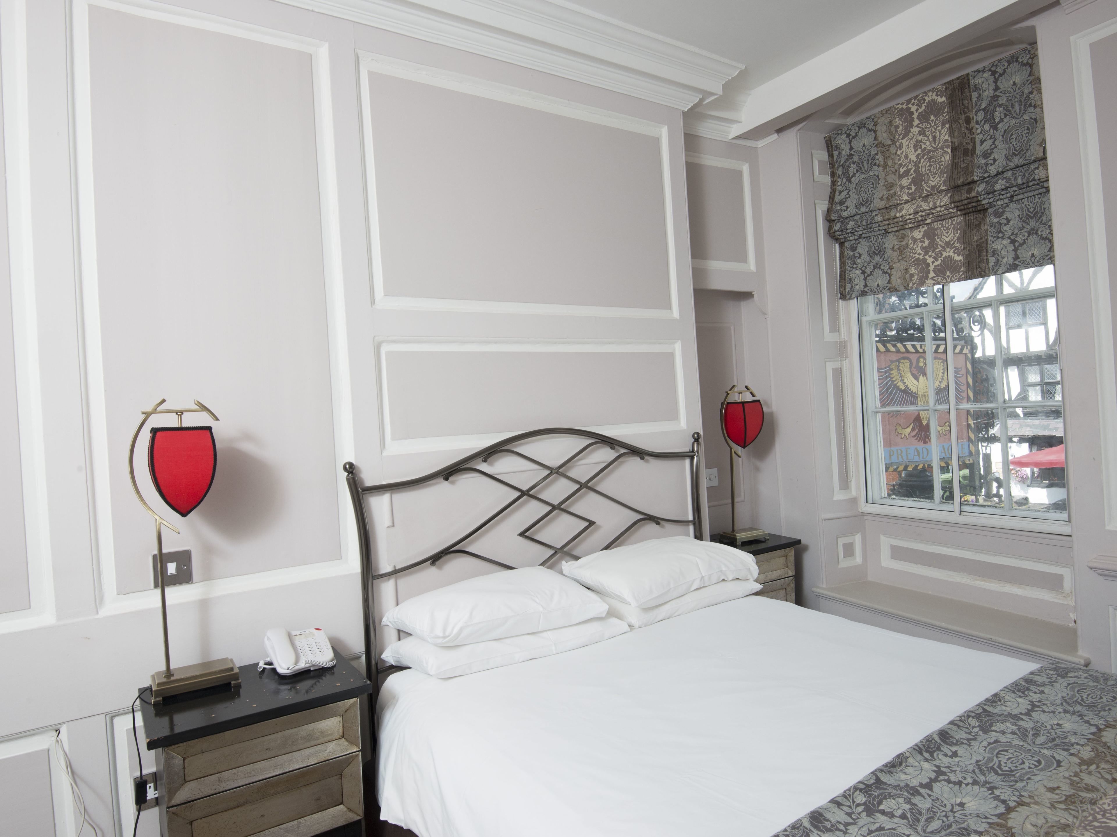 Een keurig opgemaakt slaapkamer met een bed, nachtkastjes en een raam met patroon gordijnen.