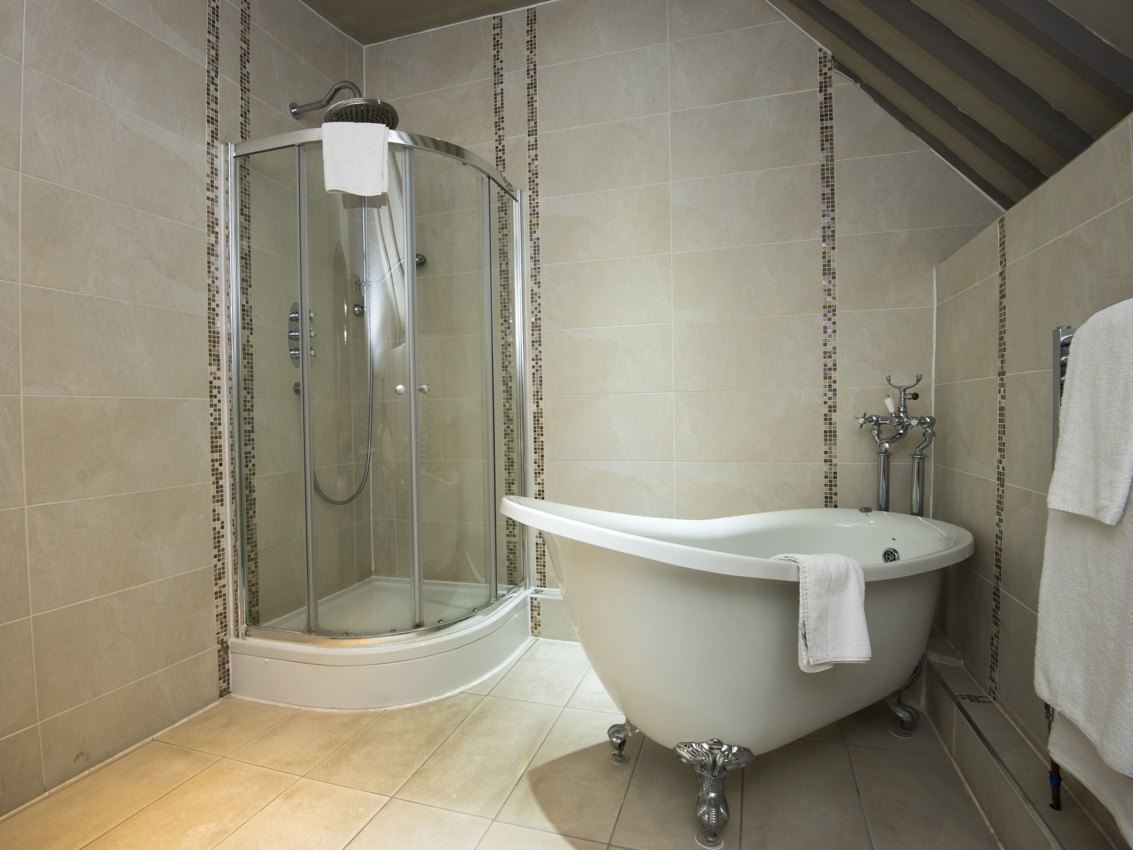 Un baño moderno con ducha de mampara de vidrio, bañera independiente y paredes con azulejos.
