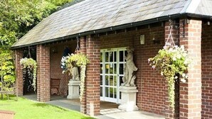 A brick building with a covered porch, stone statues, and hanging flower baskets. - The Spread Eagle Hotel (Thame)