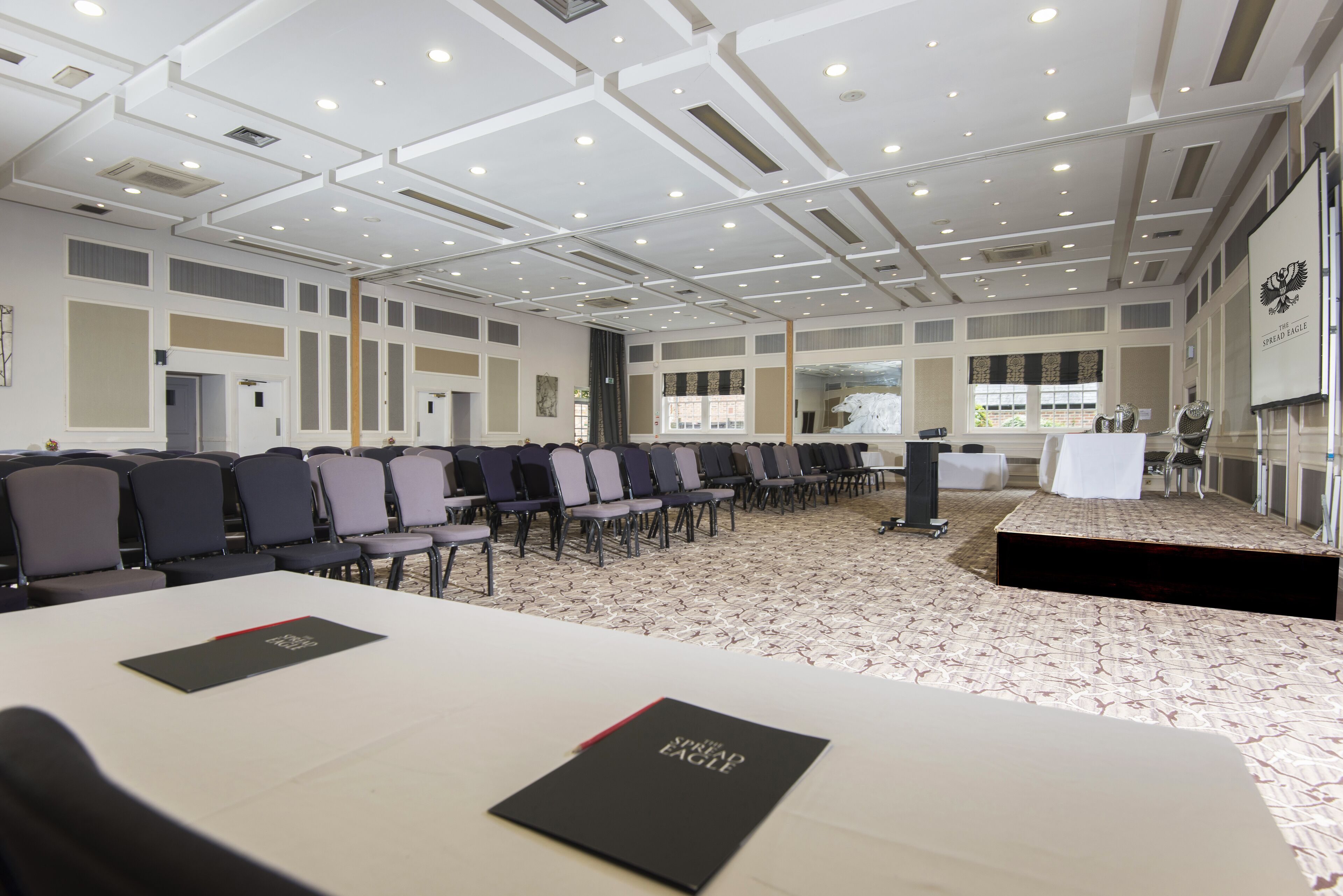 Une grande salle de conférence avec des rangées de chaises, une scène et un écran de projection.