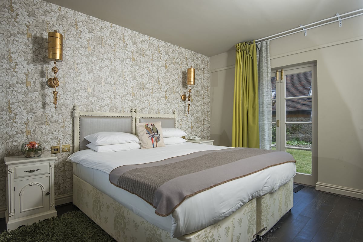 Un dormitorio con una cama grande, dos mesitas de noche, una lámpara de pared y un ventanal con cortinas.