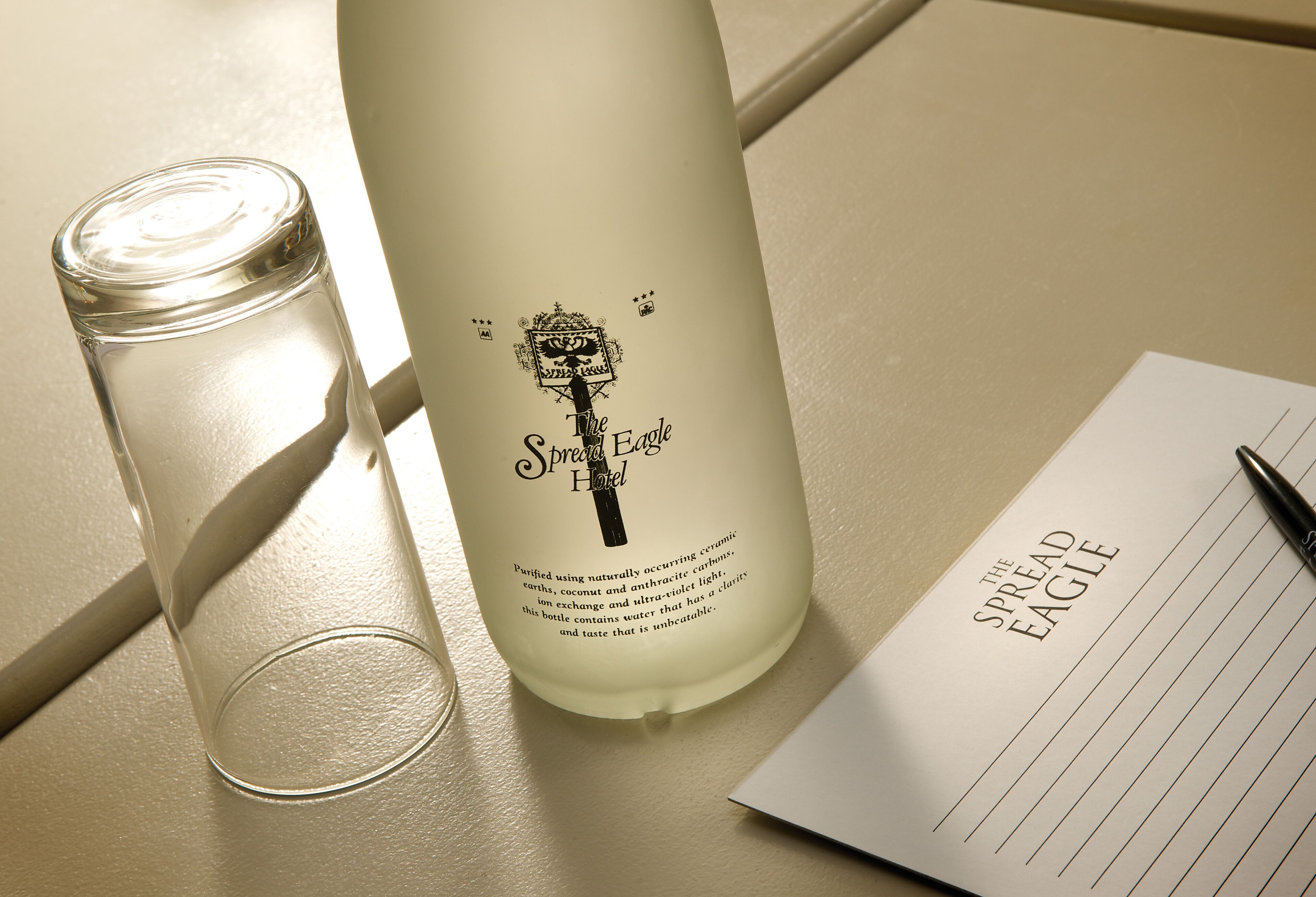 A bottle labeled "The Spread Eagle Hotel" with a candle beside it and a notepad with the hotel's name.