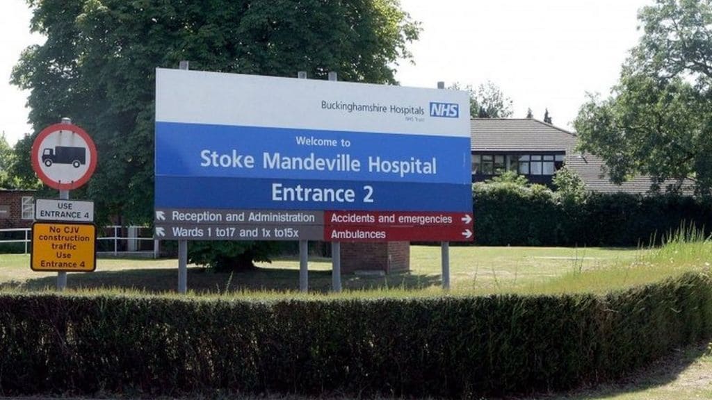 Señal de entrada al Hospital Stoke Mandeville con indicaciones hacia Recepción y Administración, Salas de 1 a 17, y Ambulancias.
