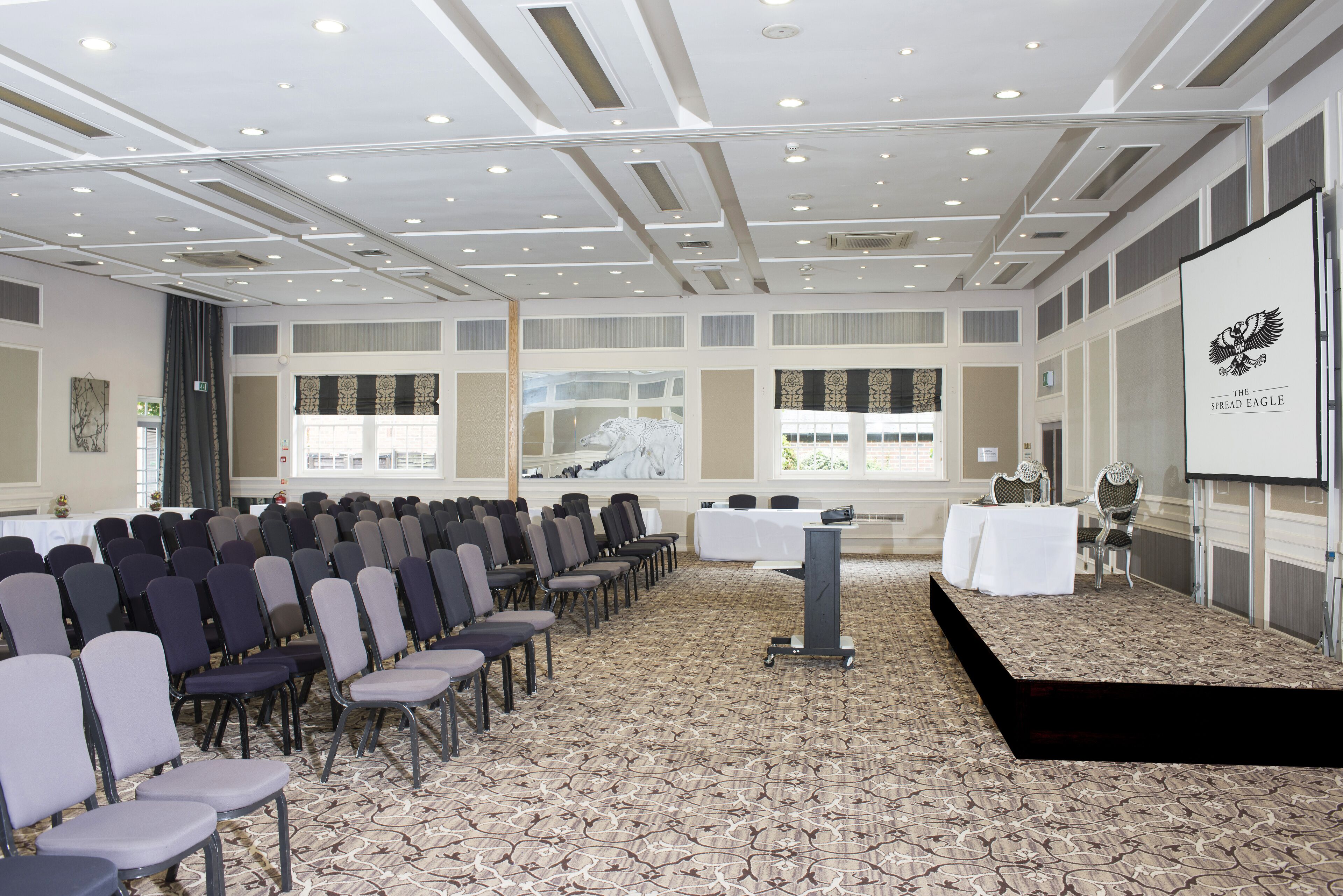 A conference room with rows of chairs, a stage, and a projection screen.