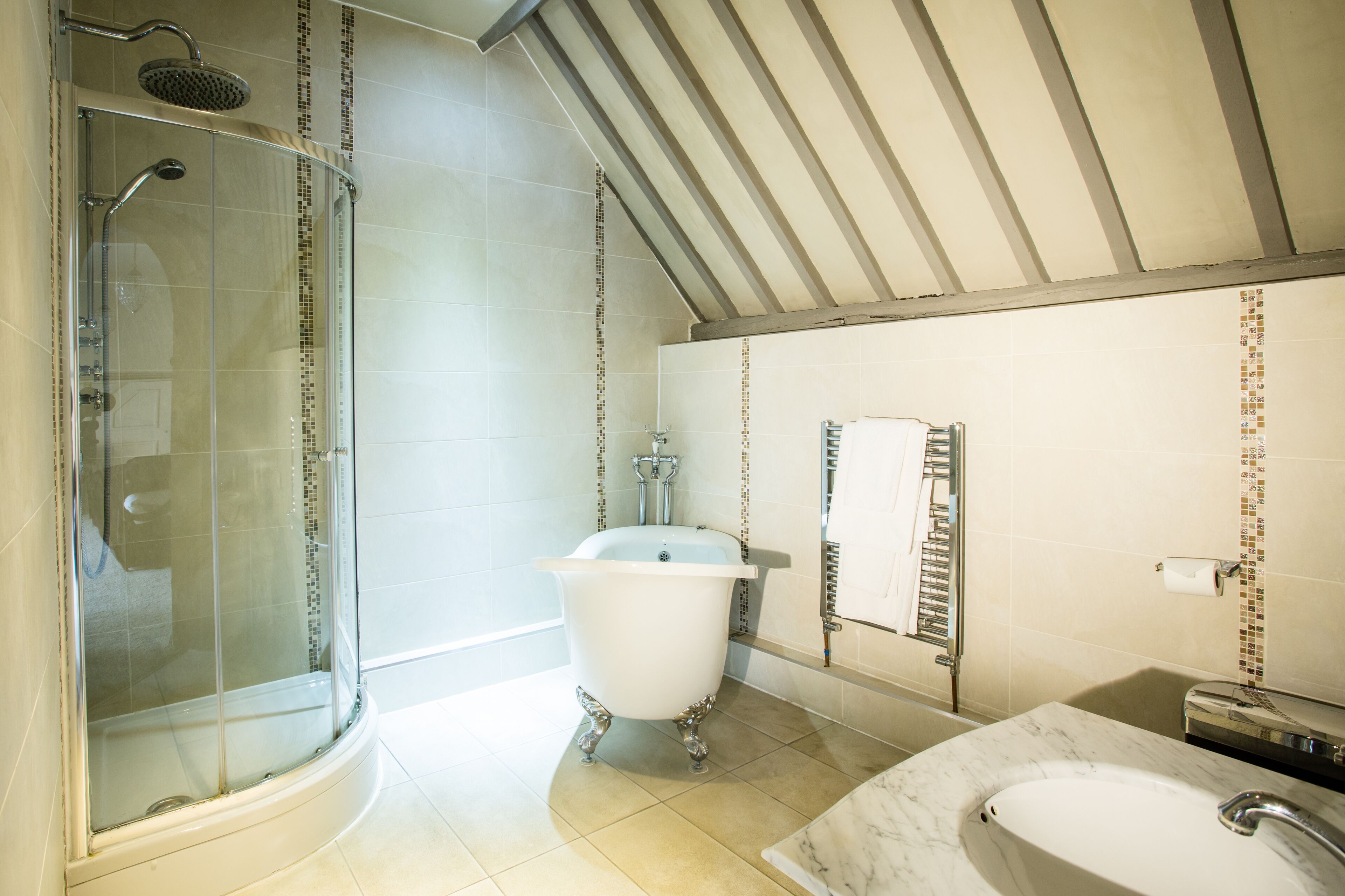 A bathroom with a glass-enclosed shower, a clawfoot bathtub, and a marble sink.
